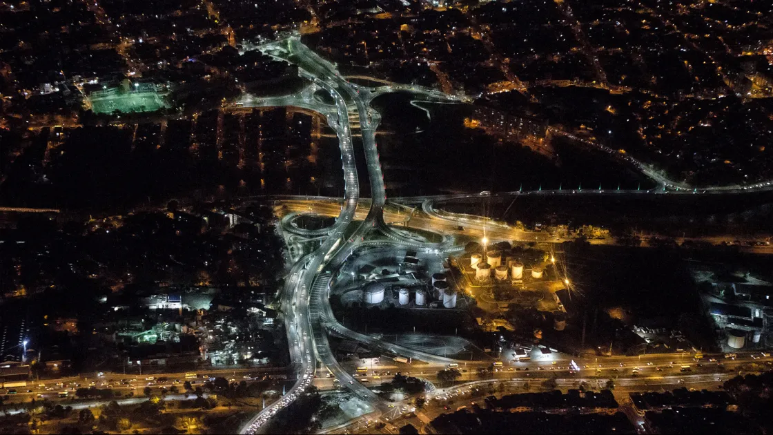 La imagen captura la magnitud del que es considerado el puente intraurbano más largo de Colombia, conectando de forma estratégica las comunas del norte (Aranjuez y Castilla) sobre el río Medellín. Las curvas de los puentes y las orejas de la intersección brillan con una intensa iluminación LED blanca, simbolizando el progreso y la conectividad de la "Ciudad de la Eterna Primavera".